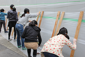 壁に立てかけた板に塗り作業をする児童