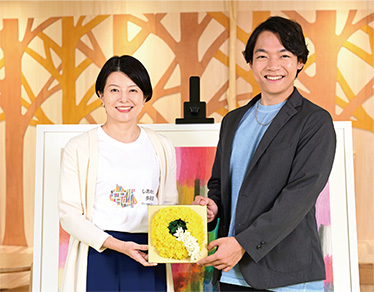 Qをかたどったお花を手に持つ森澤区長と伊沢さん写真