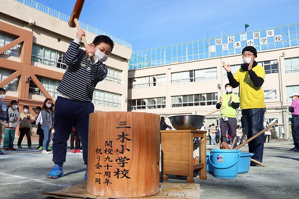 校舎をバックに餅をつく子供