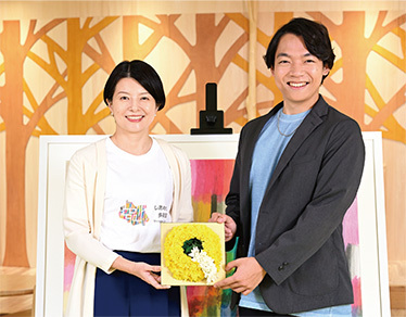 写真：Qをかたどったお花を手に持つ森澤区長と伊沢さん