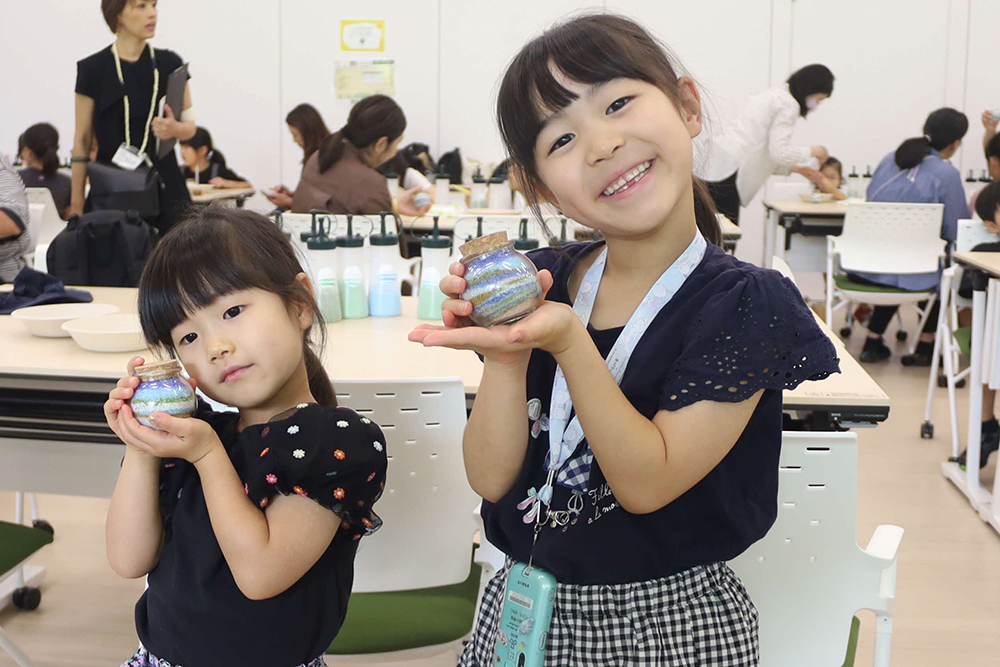 完成したクリスタルサンドアートを手にもってポーズを取っている子どもの写真