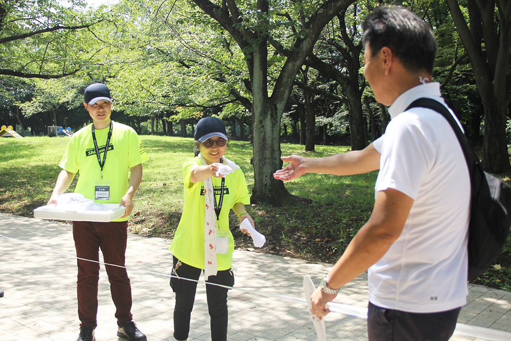 しな助が来場者へ冷やしタオルを配布する様子