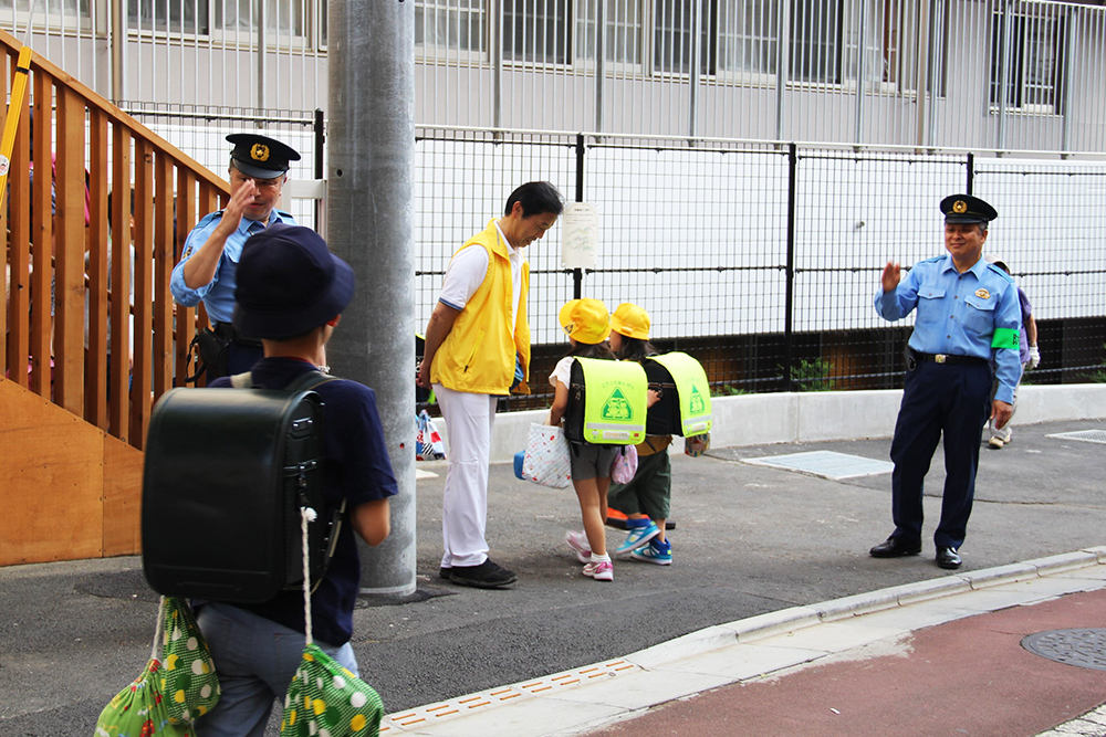 校門前で警察官と地域住民が見守り