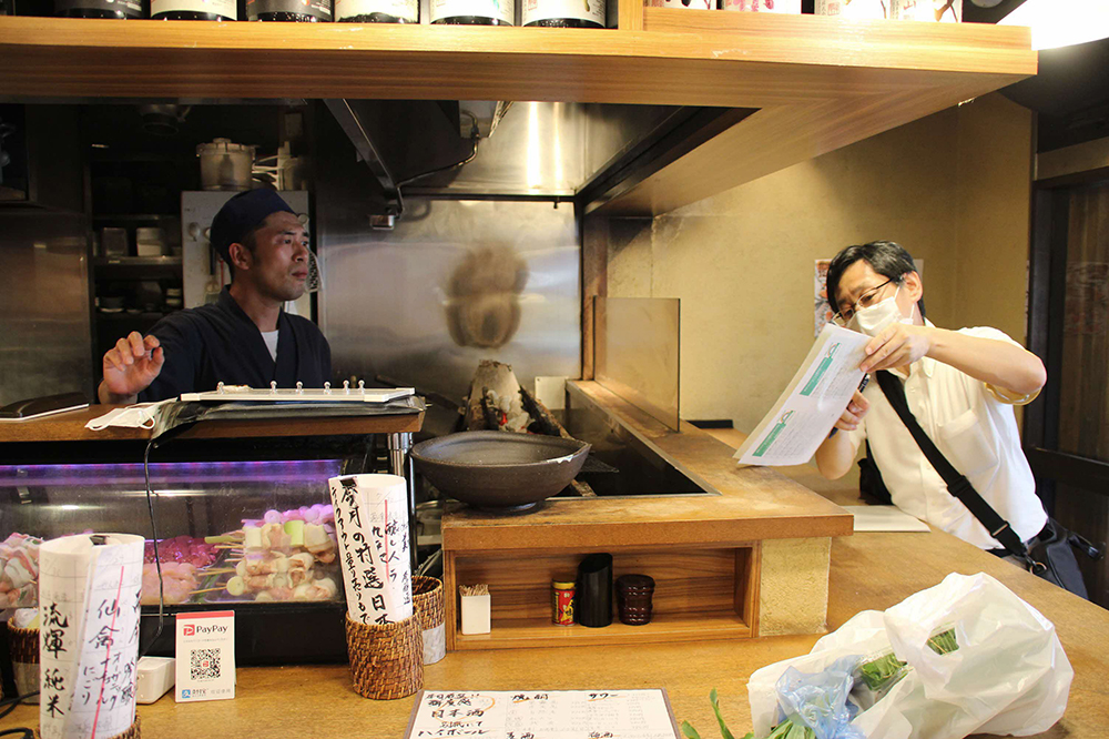 飲食店の店員に制度の案内をする職員