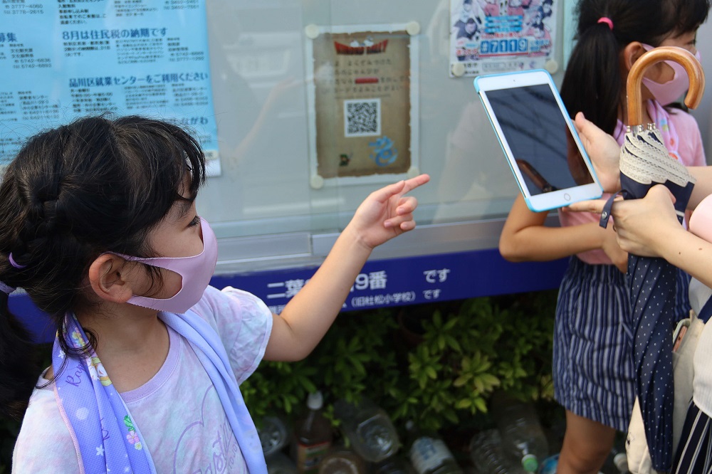 掲示板の前で携帯を指さす女の子