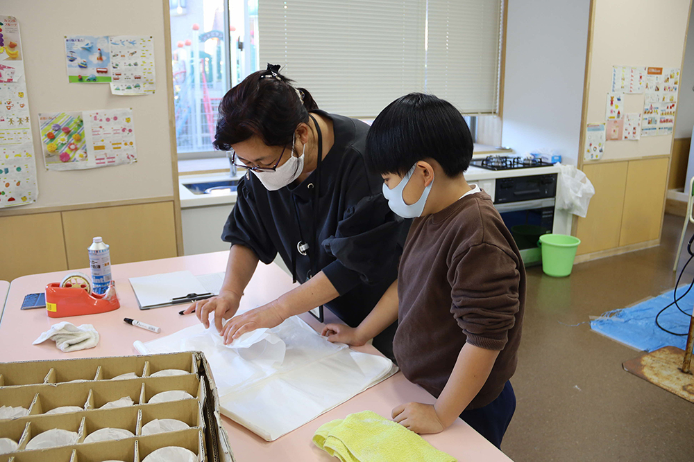 完成したグラスを包む先生とそれを見る子供