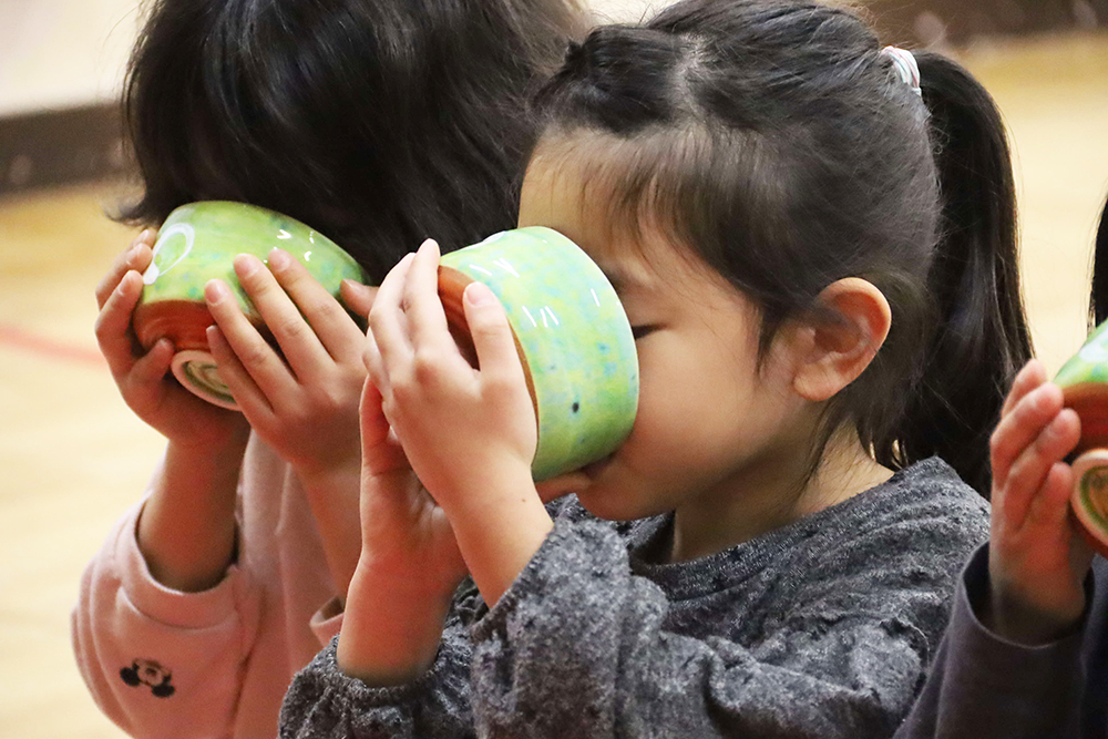 お茶碗を傾けてお茶を飲む子ども