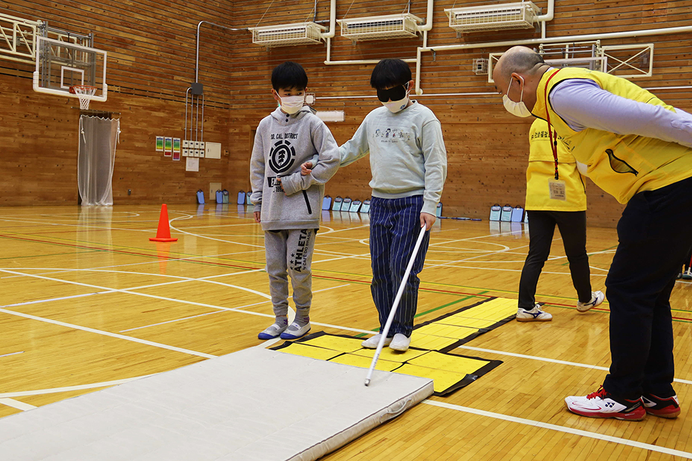 目隠しをした子どもの手を取り補助