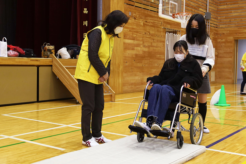 険しい表情で車いすの補助をるす女の子