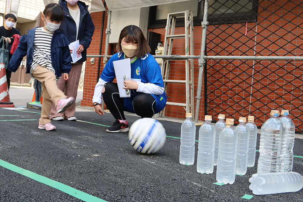 ボールを蹴ってペットボトルのピンを倒そうとする子ども