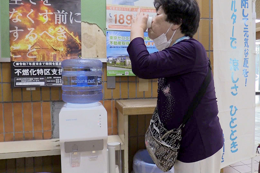 ウォーターサーバの水を飲む高齢女性