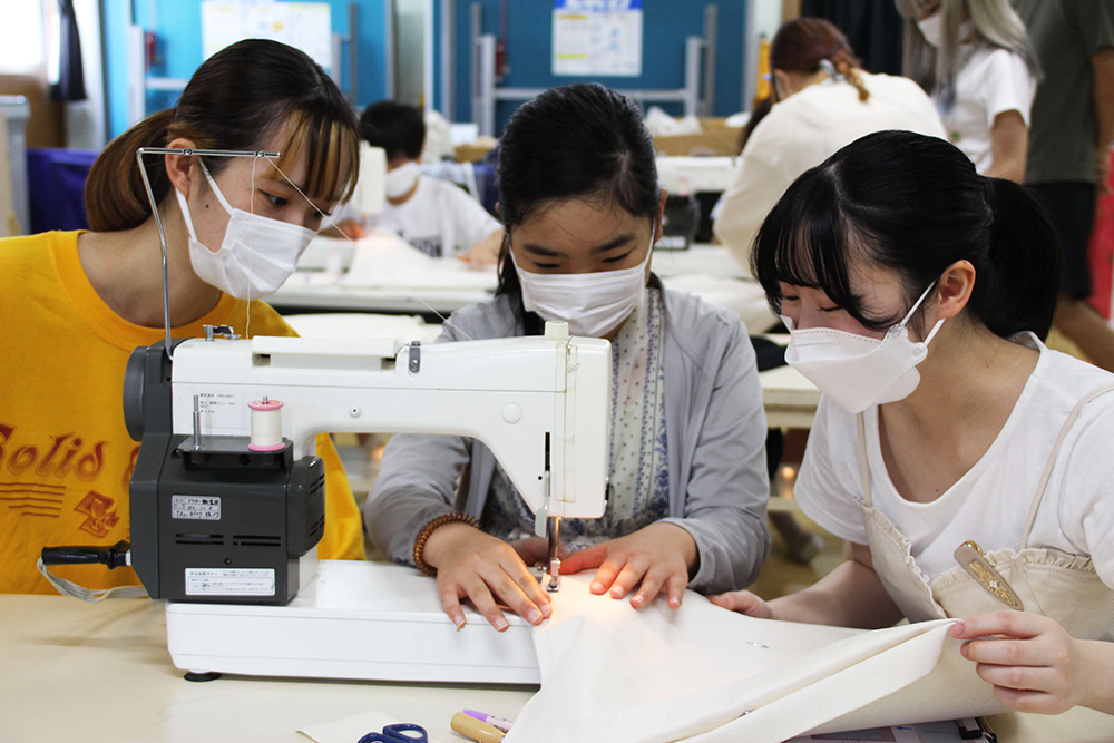 ミシンをする女の子を見守る学生