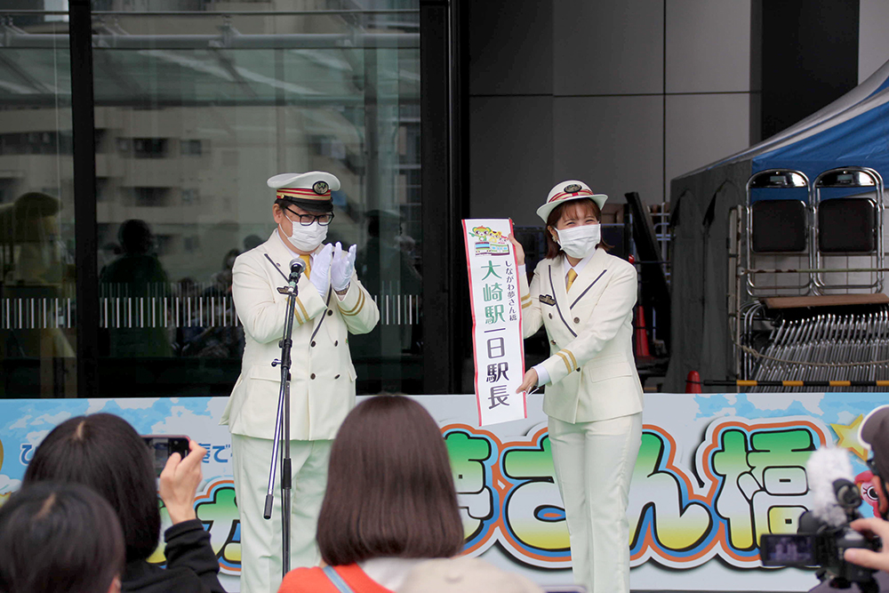 大崎駅長から山口さんに一日駅長のタスキを渡す