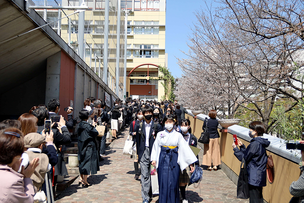 桜が咲き始めたスロープを歩く卒業生