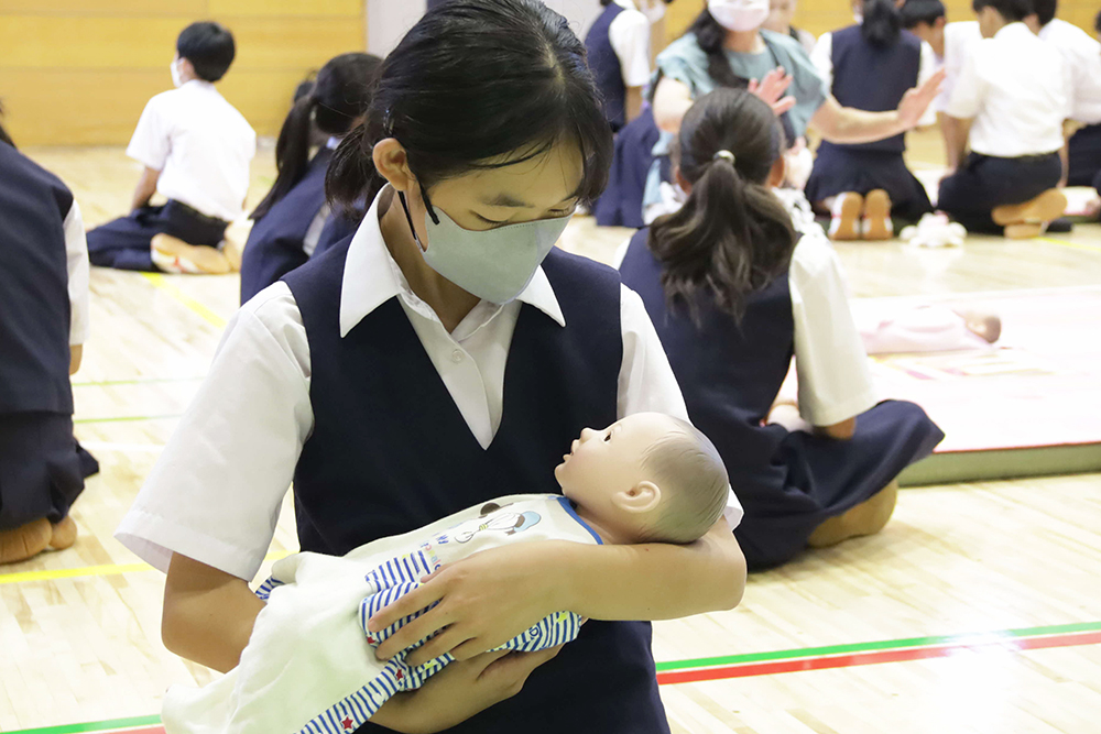 赤ちゃん人形を抱っこする生徒の全身