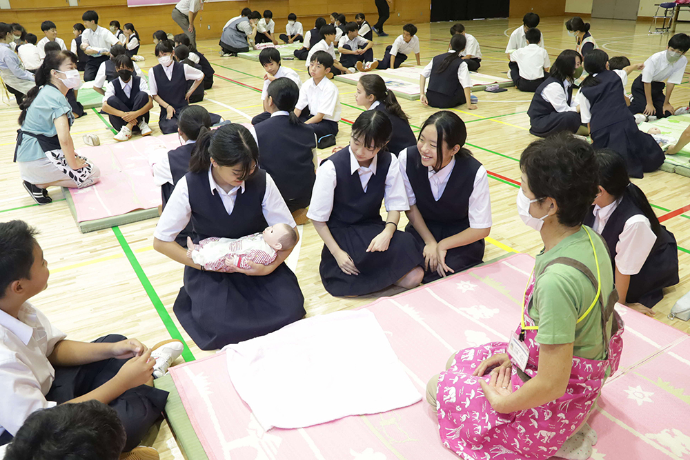 赤ちゃん人形を抱っこする生徒と見守る周りの生徒