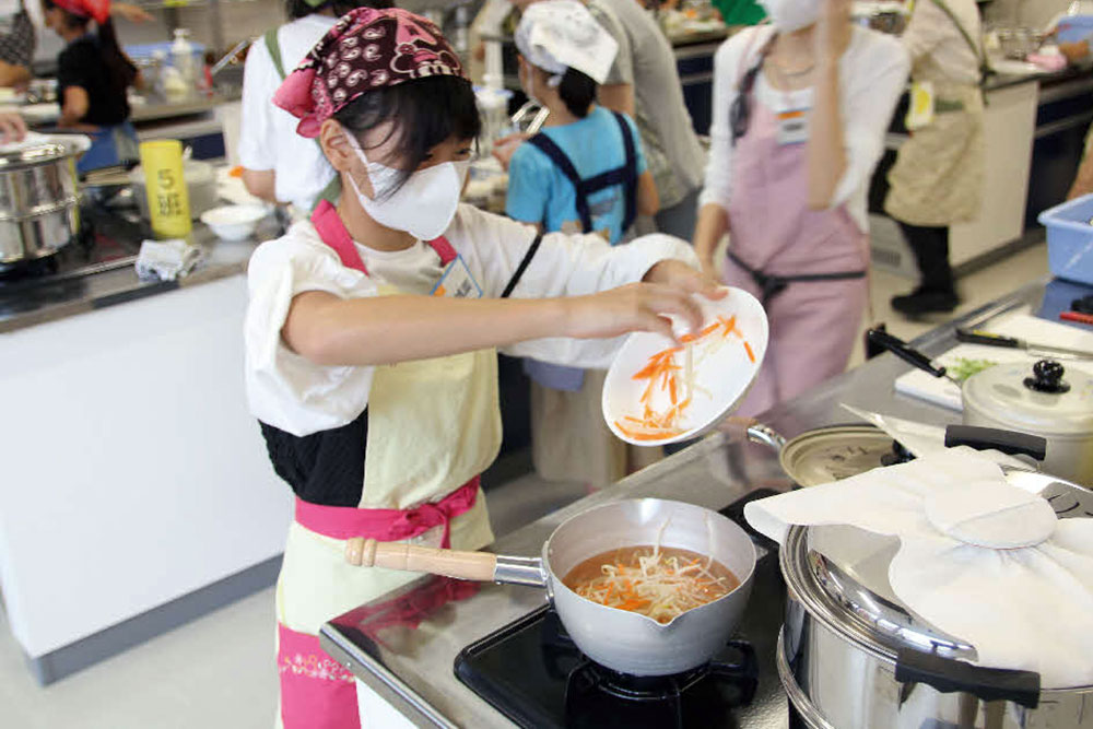 子どもが鍋に野菜を入れている写真