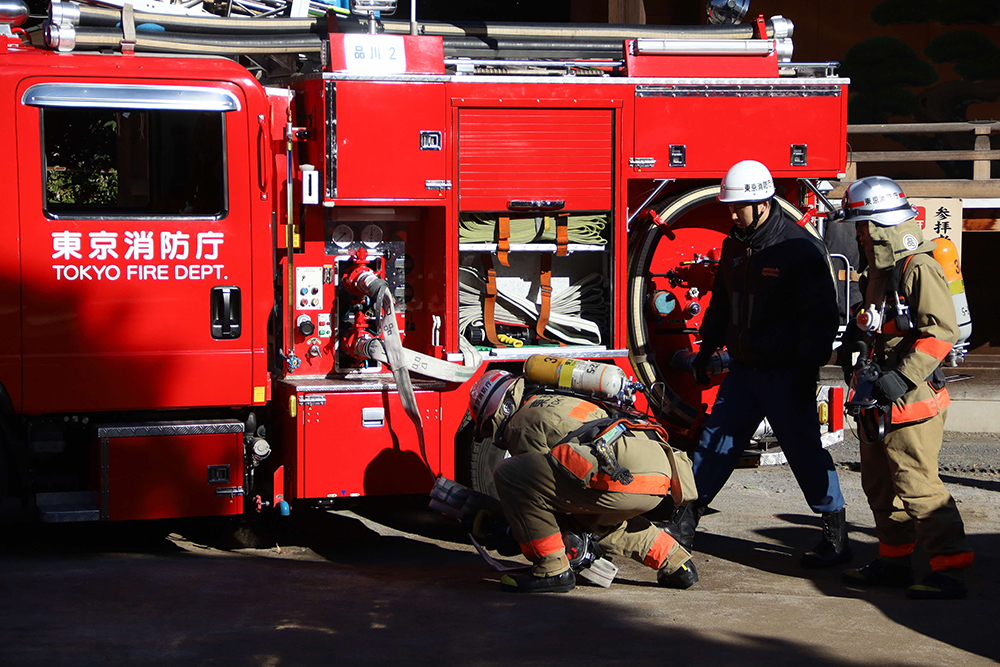 消防車からホースを伸ばす消防隊員の画像