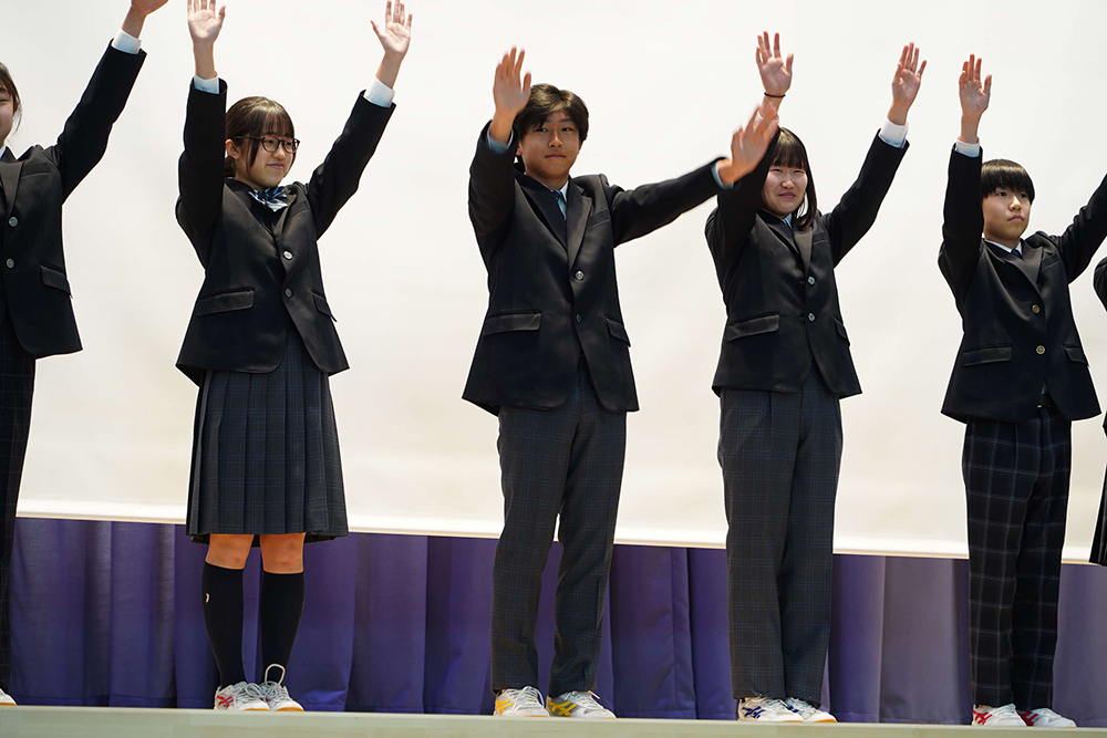 壇上で両手を挙げて制服を見せている生徒たちの画像