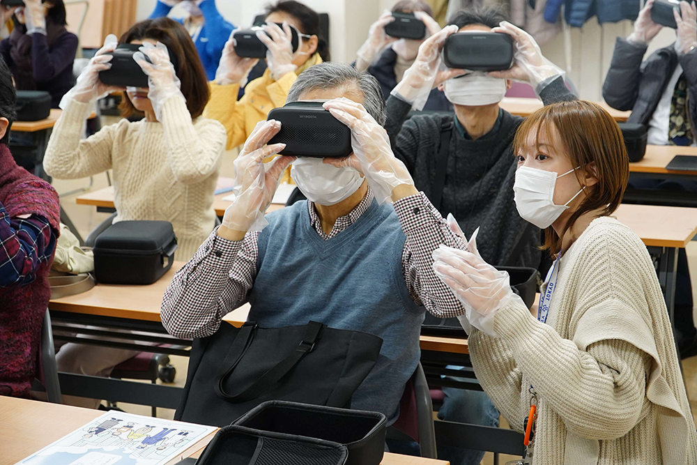 区職員の説明を聞きながらVRを体験する参加者の画像