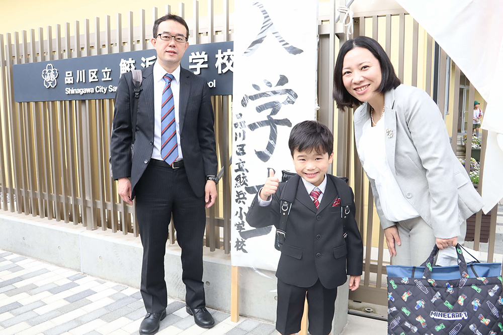 校門前で記念撮影する新入生と家族の画像