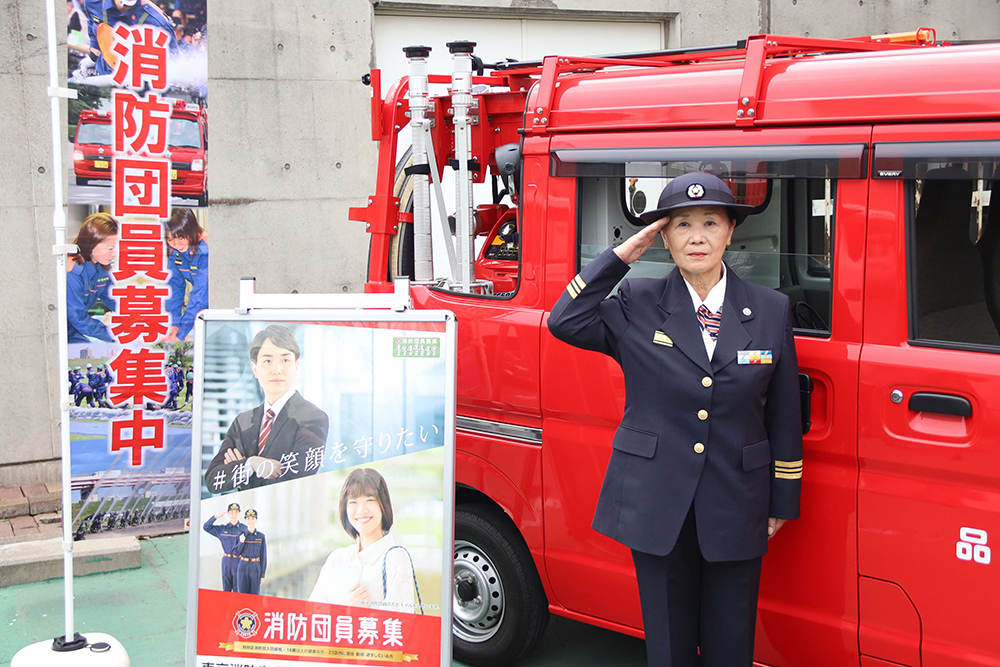 消防車の前で敬礼する女性消防団長の画像