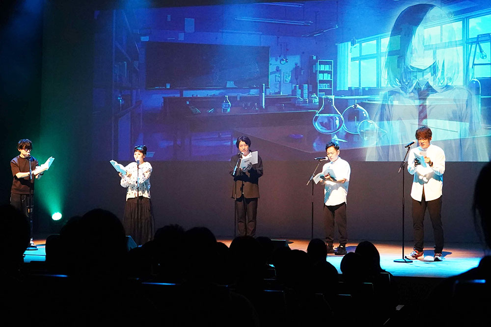 スクリーンをバックに朗読する声優の画像
