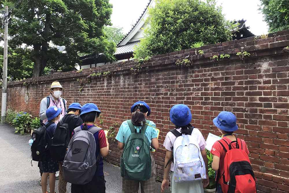 古いレンガの壁について説明するガイドと話を聞く児童の画像