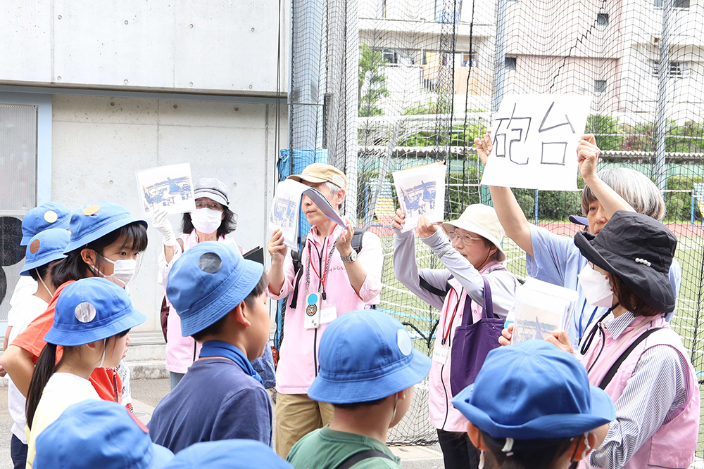 台場小周辺の歴史を話すガイドと話を聞く児童たちの画像