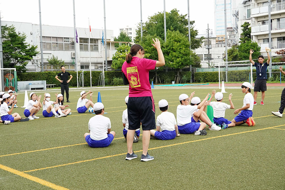 校庭で講師の話を聞く小学生