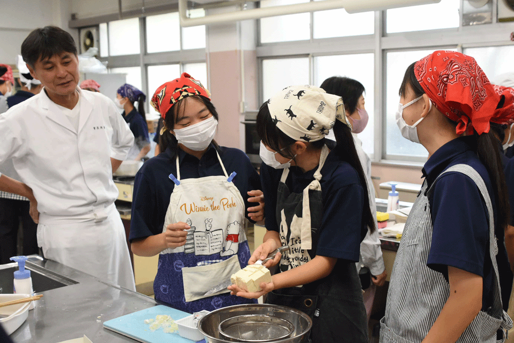 豆腐を切る女子生徒とそれを見る笠原さん