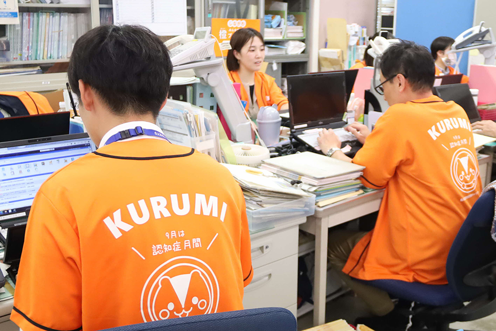 オレンジ色のTシャツを着た職員の後ろ姿の画像