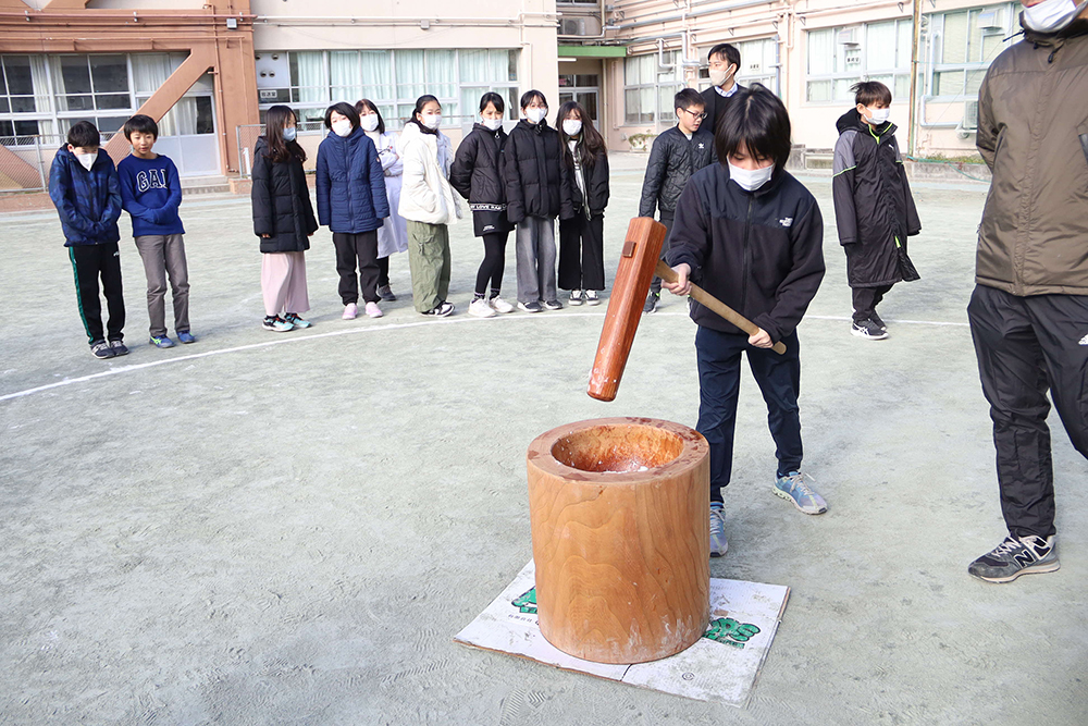 もちつきをする児童と応援する児童の画像