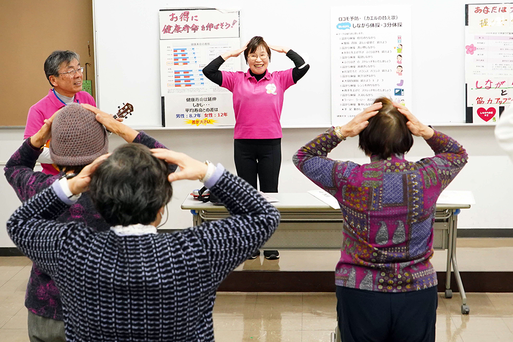 頭に手を置いて体操している写真