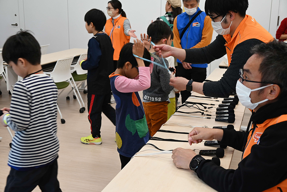 解説と録音に使うICレコーダーを首にかける子どもたちの画像