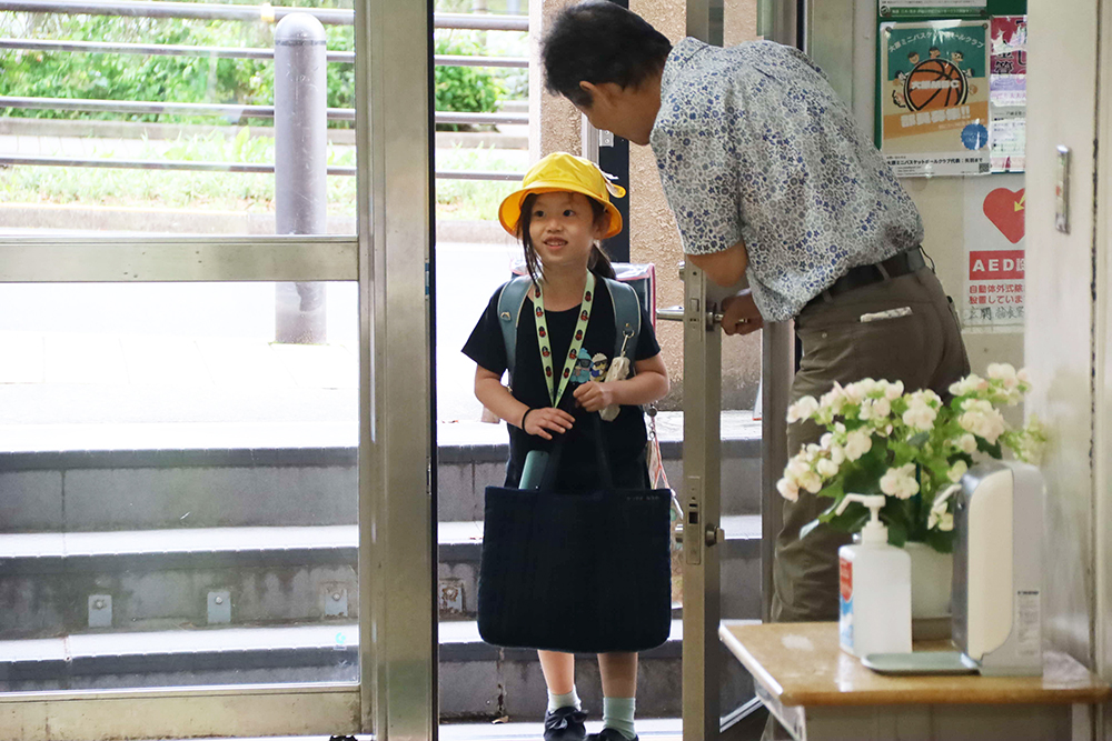 スタッフに迎えられ登校する児童の写真