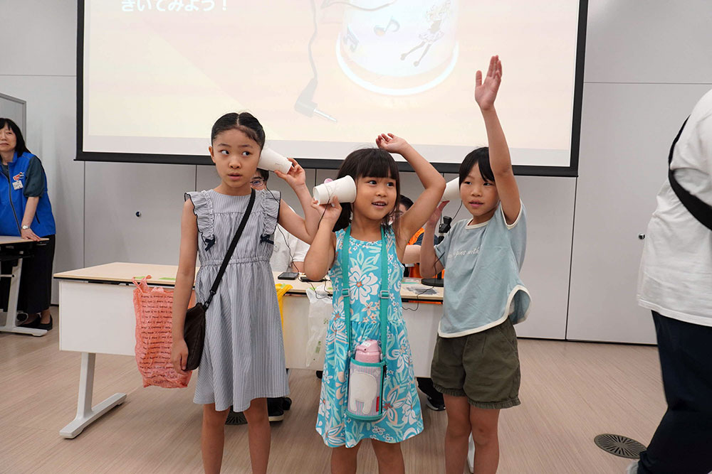 手作りスピーカーで音楽を聴く子どもたちの写真