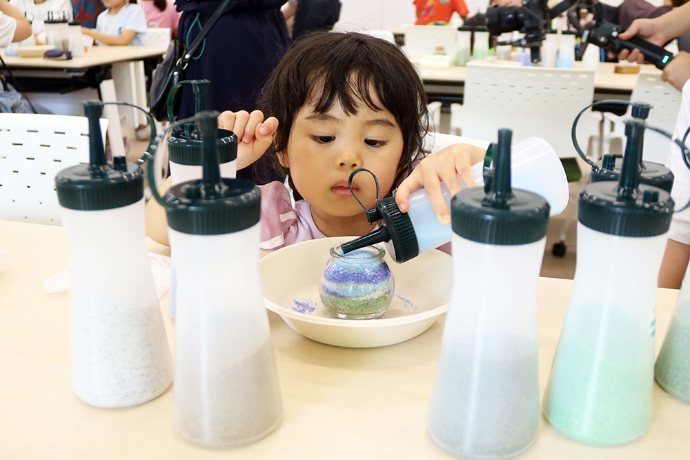 子どもが真剣にクリスタルサンドを瓶に入れている写真