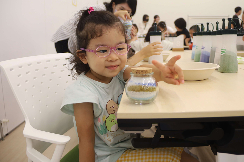 子どもが完成したクリスタルサンドアートと記念撮影している写真