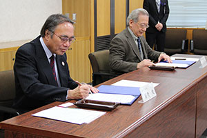 協定書にサインをする区長と学長