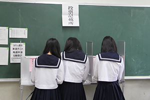 投票記載台で候補者名を記載する生徒
