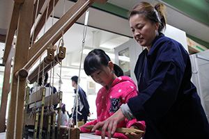 丁寧に手織物機の操作を指導する藤山優子さん
