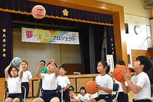 座ったままボールを投げる3人の児童