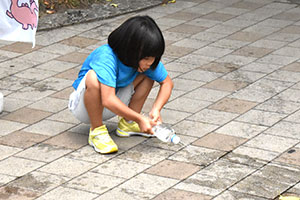 乾いている地面に水を撒く子ども